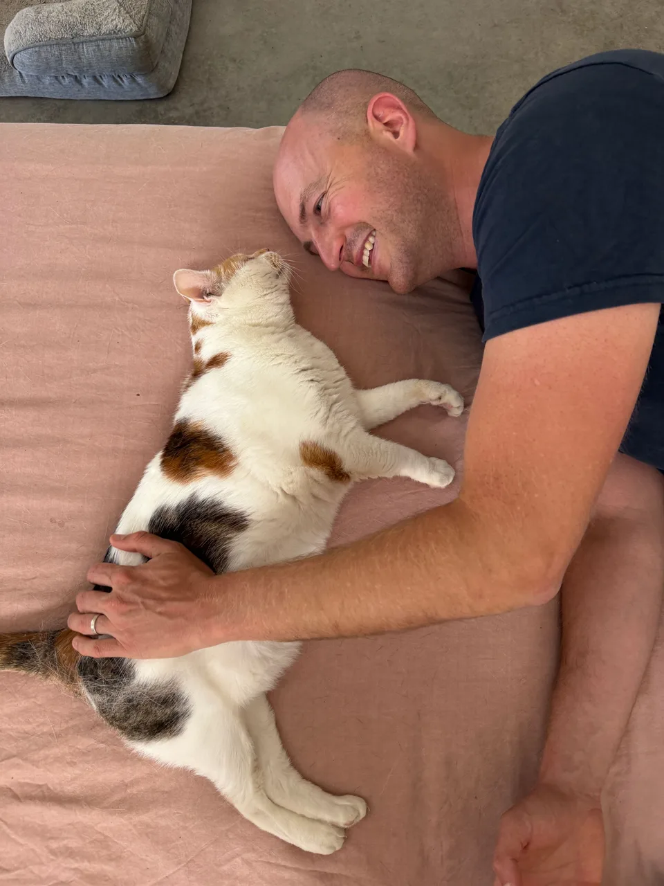 Kyle smiling beside a relaxed cat on the sofa