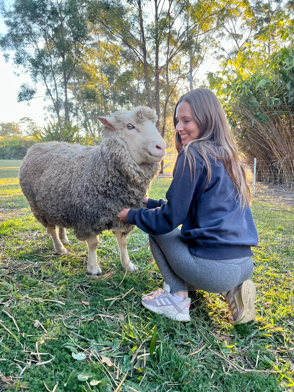 A woman crouching in the grass to spend time with a sheep