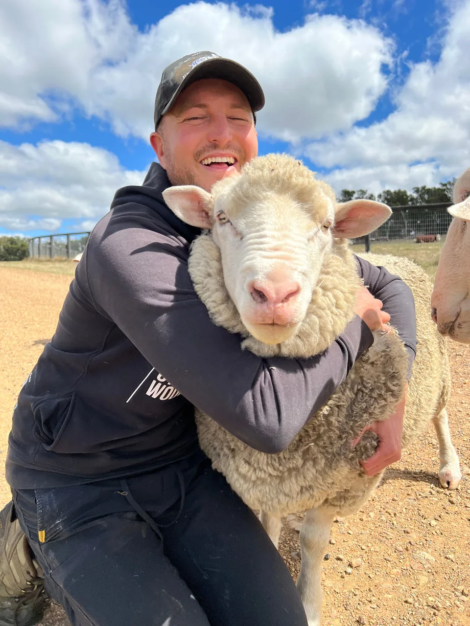 Kyle wrapping his arms around a sheep outdoors