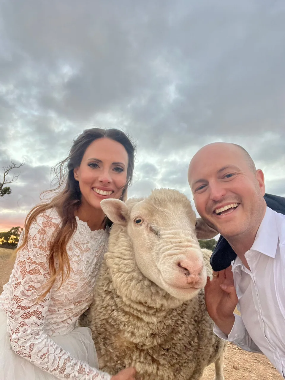 Kyle and Kelly in wedding clothes, smiling beside a sheep
